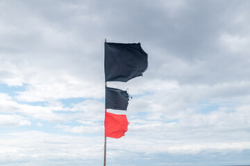 Black and red flags on cloudy sky.