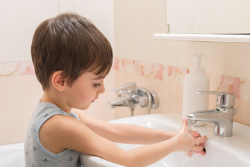 A little boy washes his hands with soap and water in the sink.