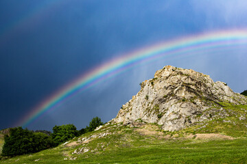 Beautiful strong rainbow against dark sky over a huge rock