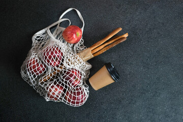 Beige mesh bag with fresh apples, bread and a glass of coffee in kraft packaging on a dark background. Purchases. Waste-free, eco-friendly or plastic-free lifestyle, copy space

