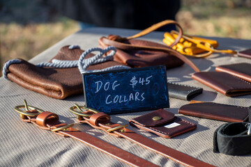 Hand crafted dog collars and other leather goods for sale on a tabletop at an outdoor market.