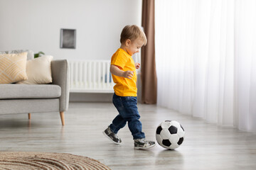 Future champion. Adorable little toddler boy playing football, hitting ball at home, having fun in...