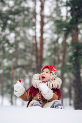 Child girl has fun with lollipop in hand and bagels bunch on her neck in snowy forest.