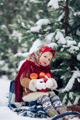 Little child girl plays with apples during the walk in snowy forest.