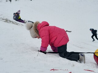 A girl climbs a mountain in the snow on the descent to ride rubber tubes. Clear frosty winter day.