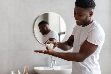 African Man Squeezing Liquid Soap From Bottle In Bathroom