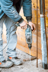 Worker using a drilling rotary power tool on construction site and creating holes in concrete