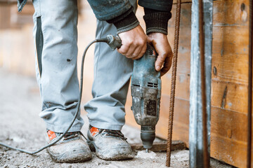 Builder working with rotary hammer drill equipment making holes in concrete on construction site