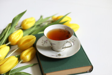 A cup of tea and bunch of yellow tulips on white background. Concept of holiday, birthday, Easter,...