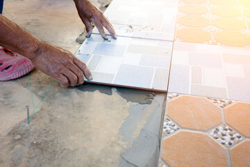 The hands of the tiler are laying the ceramic tile on the floor in construction site