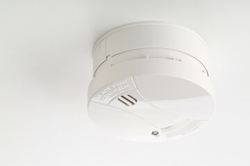 Smoke detector or fire alarm sensor on white ceiling background, house safety or security concept