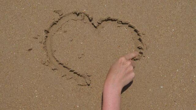 Happy tourist woman draw heart on wet sand using pointer finger, top-down view. Tourist enjoy carefree holidays at exotic island of Thailand