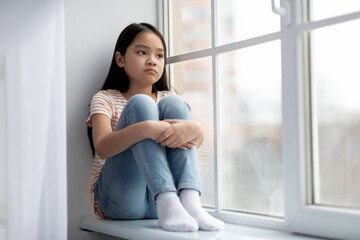 Bored asian girl sitting on windowsill alone, copy space