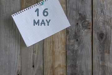 Day of month.A white sheet of checkered paper from a notebook with a date is pinned with a stationery button to a wooden background.