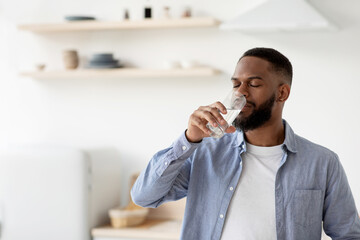 Fototapeta Calm young african american male with beard drinks of clean water from glass with closed eyes obraz