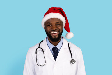 Handsome black doctor in uniform and Santa hat posing over blue background