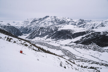 Panoramic view of the Italian Alps with snowy peaks and the town of Livigno on a cloudy day