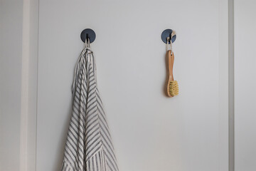 Gray bathrobe and a wooden body brush hanging on black hooks on a white door in a modern design bath room. Eco friendly sustainable, recyclable beauty accessory. Minimalistic green slow living.