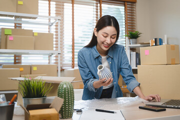 Young Asian woman owner of small online store packing customer orders in the home office.