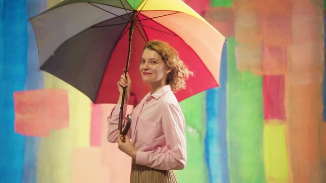 Lovely slim girl posing with sincere smile. Amazing cool smiling girl on the rainbow background. Beautiful woman holding multicolored umbrella.