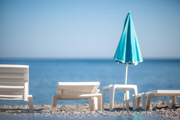 Several white sun loungers and a turquoise parasol on a deserted beach. The perfect vacation concept.