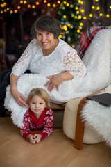 Cute child and grandmother, sitting on a cozy armchair at home on Christmas, playing together