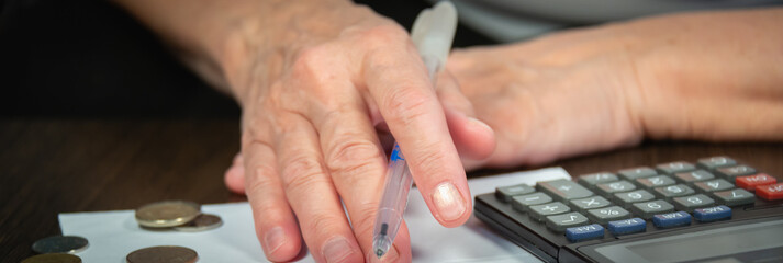 A woman is counting expenses and income on a calculator. In the hands of a pen and small metal...