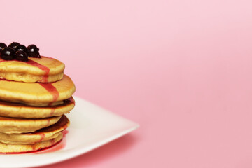 Cropped stack of pancakes with blackcurrant at the top, pink background. American tasty pancakes with berries. Closeup, copy space