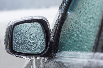 Ice-covered car mirror with icicles, glass and side doors. Icing vehicle on a winter day after...