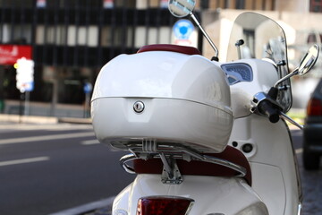 White  scooter on the street.  Luggage bag