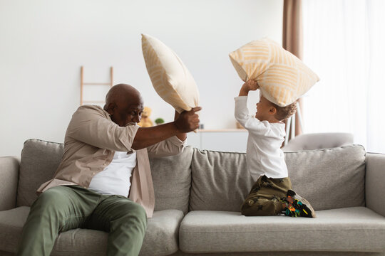Black Grandfather And Grandchild Having Pillow Fight For Fun Indoor