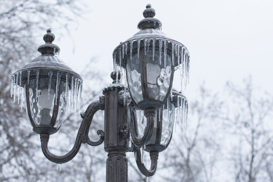 Ice-covered street light with icicles. Icing city park on a winter day after freezing rain in Mykolaiv.