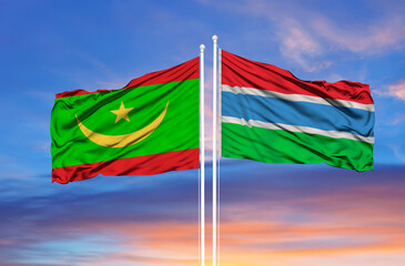 Mauritania and Gambia two flags on flagpoles and blue cloudy sky