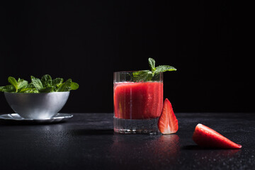 Un vaso de refrescante jugo de fresa triturado decorado con una rama de menta y fresas cortadas sobre un fondo negro © R. Guas