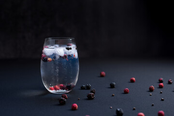 Vaso de gin tonic con moras rojas y negras sobre fondo negro