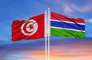 Tunisia and Gambia two flags on flagpoles and blue cloudy sky