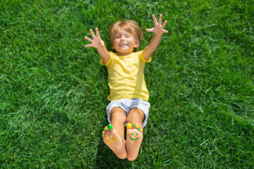 Happy child with smile on feet lying on green spring grass