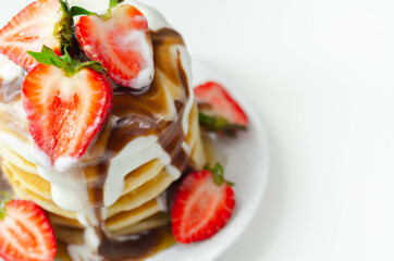 Pancakes stacked with strawberries, topped with  chocolate sauce and yoghurt