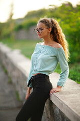 stylish young woman posing while wears a glasses in summer bright hipster clothes in the park