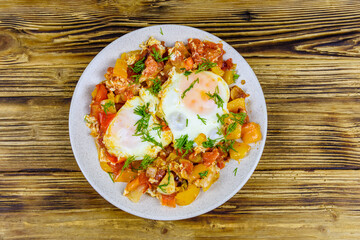 Homemade breakfast shakshuka with fried eggs, onion, bell pepper, tomatoes and dill on a wooden table. Jewish cuisine. Top view