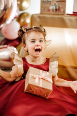 Vertical portrait of cheerful two year old baby girl in a red dress with her birthday gift