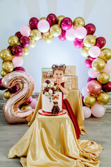 Vertical portrait of sweet two year old little girl standing behind her birthday cake and making a wish