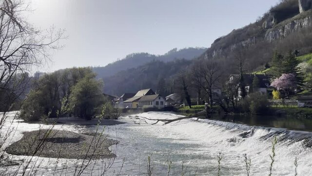 View of the Saint-Ursanne waterfalls with a fallen trunk, in the Doubs river in a park