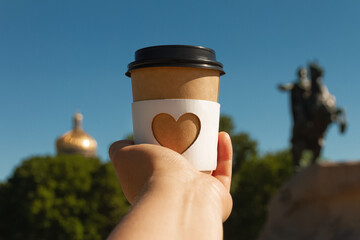 cup of natural coffee with carved white heart in woman's palm on background of Bronze Horseman in St. Petersburg, Russia