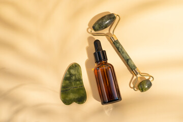 Roller and gua sha massage scraper and beauty product on a beige background with leaves shadows....