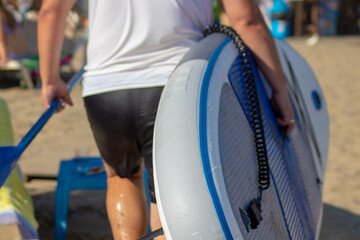 Surfer trägt sein surfbrett am strand unter dem arm, nachdem er mit nassen sachen, aus dem Wasser gekommen ist.  - obrazy, fototapety, plakaty