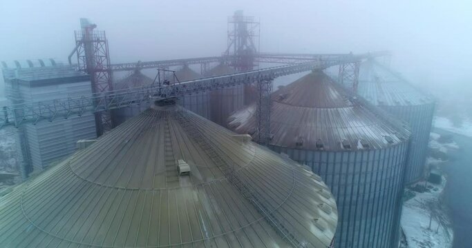 The rounded tops of the silo tanks. Drone shot over the modern grain elevators on foggy weather. Impressive granary constructions from aerial perspective.