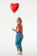 Full-length portrait of a woman in blue jeans and a red T-shirt with a heart-shaped balloon on a white background. Happy Valentine's Day