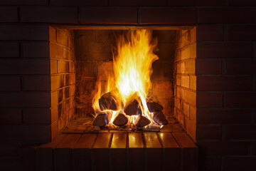 A stack of firewood burns with a bright hot flame in a red brick fireplace on a late dark cold...