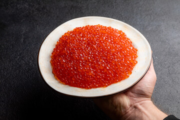red caviar on a white plate, dark background, delicacy red caviar